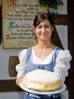 Das Bild zeigt eine Frau in Tracht, die einen Eierkuchen präsentiert.